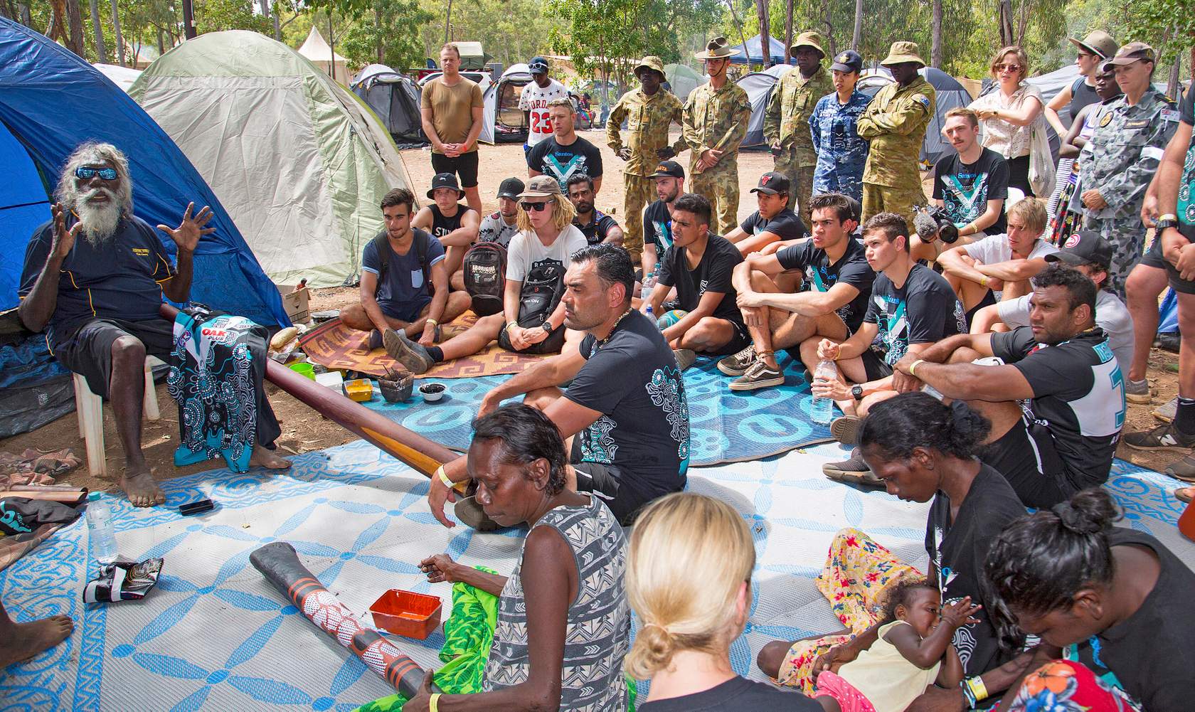 Navy, Army and Air Force members gather to hear the history of the didgeridoo told by one of the local indigenous elders during the 20th Anniversary of the Garma Festival.